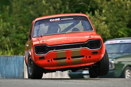 John McCoy (1969 Ford Escort Twin Cam) gets two wheels in the air rounding Mission's Turn 3 attempting to stay ahead of Alan McColl in his Ford Lotus Cortina. - Tony Ioannou photo